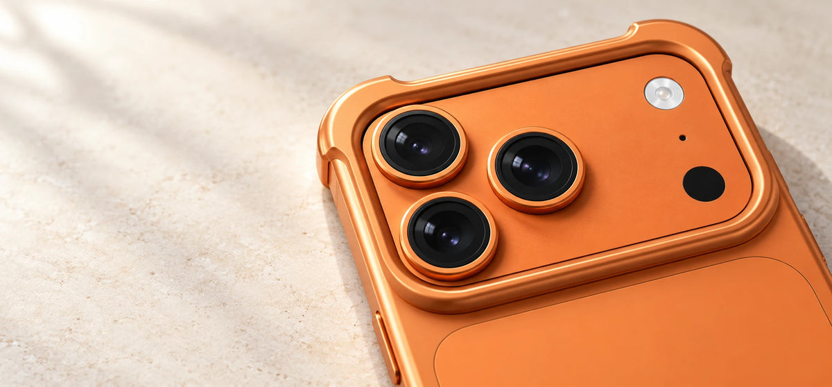 Close-up of an orange aluminum camera guard with raised corners around three rear lenses.