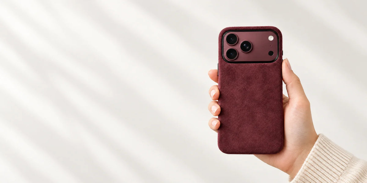 A hand holding a Burgundy fabric phone case with a matching Burgundy phone and black camera rim.