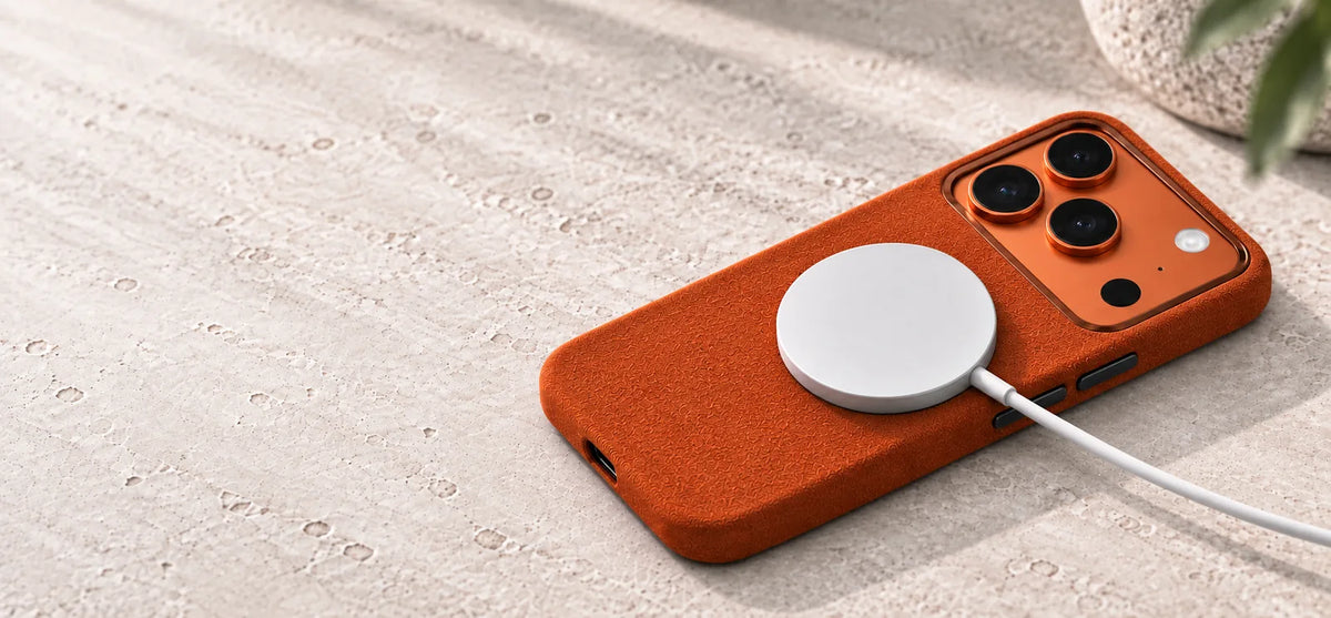 Orange fabric phone case with a copper metal camera rim and an attached white magnetic charger.