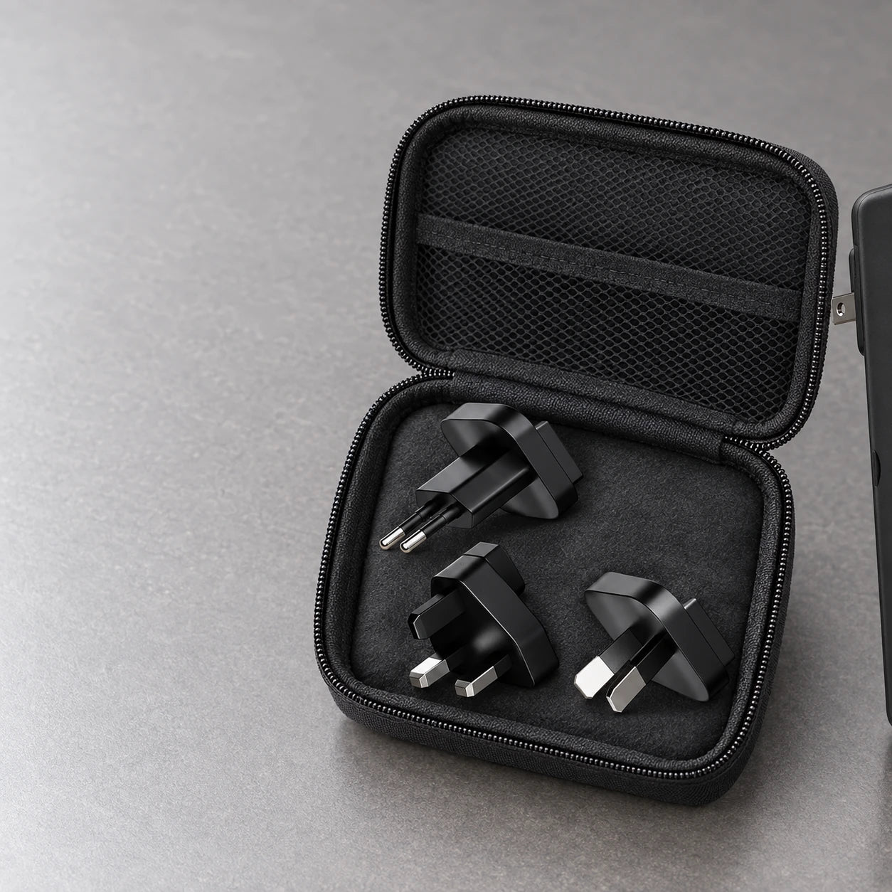 Three matching plug adapters beside the edge of a black power bank in a travel pouch.