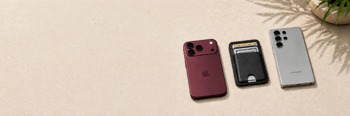 Black magnetic card wallet between a burgundy phone and a silver phone on stone.