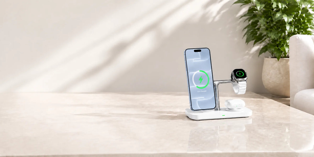 White wireless charging station holding a light blue phone, watch and earbuds on a stone desk.